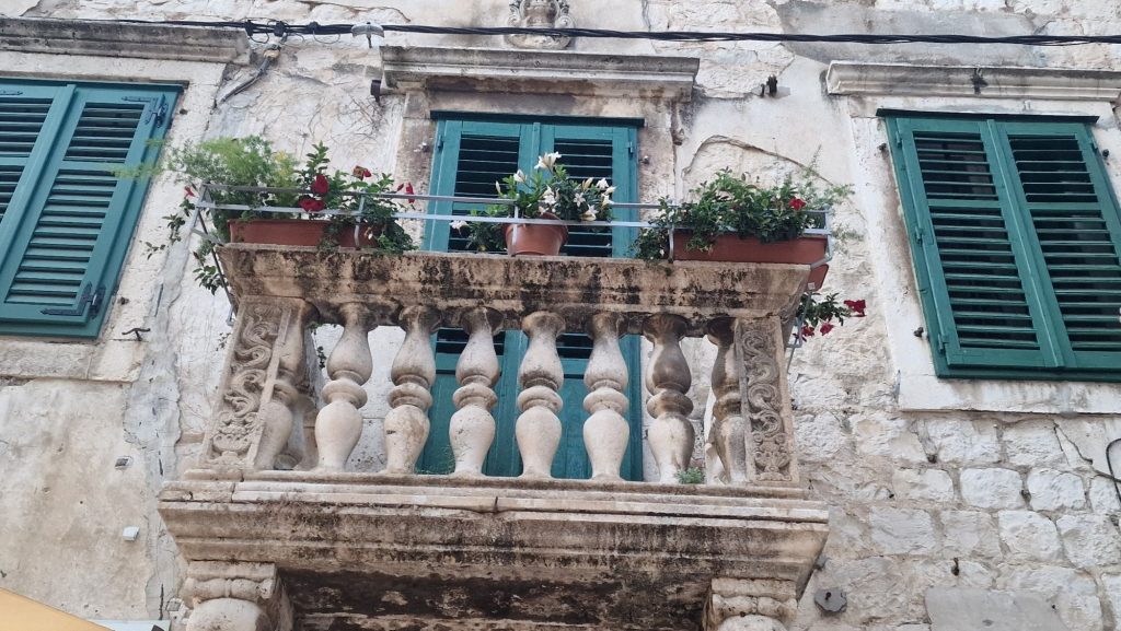 Alter Balkon mit grünen Fensterläden und Blumen in Split