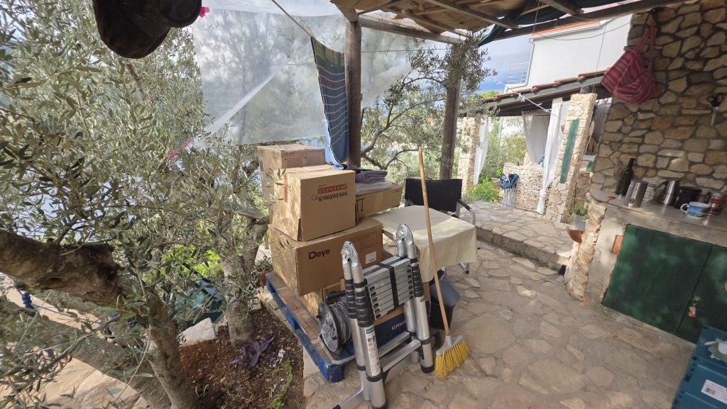 Terrasse mit Kisten, Leiter und Besen neben Olivenbaum