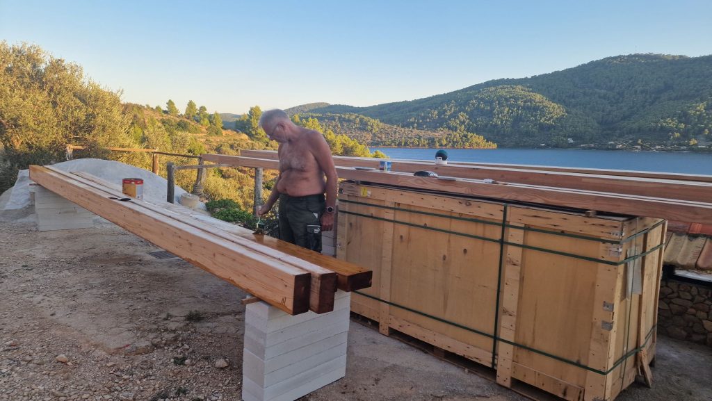 Holzbalken aufgeständert, Person streicht mit Pinsel im Abendlicht