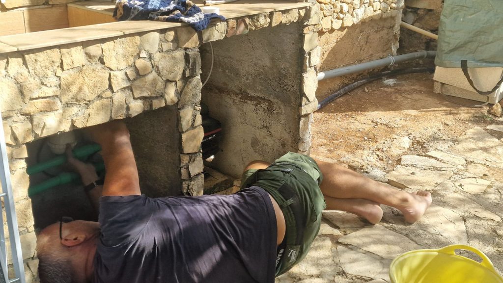 Arbeiten unter der Spüle der Außenküche mit grünen Rohrleitungen